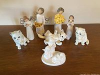 Photo showing four Willow Tree angel figurines with various poses, accompanied by three Goebel white cat figurines and one Goebel rabbit figurine on a floral base.