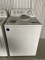 Front view of a white Amana top load washing machine with control panel and a glass lid, showing the overall condition and dials.