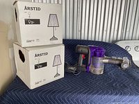 Photo shows two IKEA ÅRSTID lamp boxes and a Dyson DC34 Animal handheld vacuum cleaner.