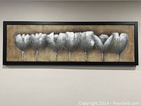 Front view of framed art showing seven silver leaf designs on a gold background with a black frame