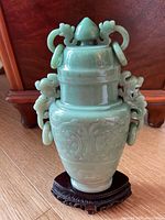 Full front view of celadon jade vase on wooden stand against wood flooring