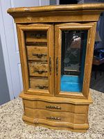 Front view of wooden jewelry box showing multiple drawers and glass door with floral etching