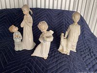 Three Lladro porcelain figurines: a kneeling boy, a standing girl, and a standing boy with a toy horse.