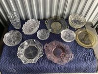 Overview photo of miscellaneous crystal and glassware items on a blue quilted cloth showing bowls, trays, plates, and a tumbler glass.
