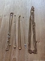 Lot of five jewelry items laid out on wooden floor including chain necklaces, bracelet, and pendants.
