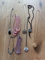 Seven various necklaces and strands arranged flat on wooden surface showing different styles including beaded and pendant necklaces.