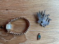 Three jewelry items including a Gruen watch, bird-shaped brooch, and small turquoise pendant on a wooden surface.