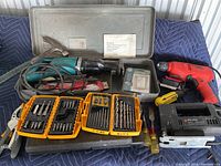 Wide view showing all items including tools and accessories in and around the grey Makita case on a blue padded surface.
