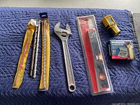 Photo of assorted tools laid on a blue quilted surface including saw blades, an adjustable wrench, a level, a laser measuring device, and a bit set.