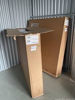 Two large cardboard boxes containing parts for a Zedbed adjustable bed, one box open at the top, stored in a metal storage unit.