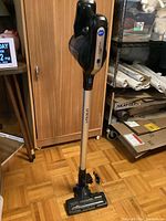 Full view of the Airstream cordless stick vacuum showing the vacuum in upright position with charger plug on floor.