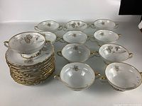 Full set view showing stacked plates and soup bowls with handles, gold rim, and floral decoration.
