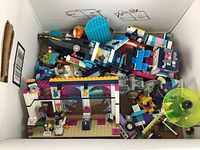 Top view of a box containing assorted modern LEGO pieces including partially built structures and minifigures.