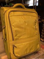 Front and side views of yellow-green Delsey Luggage rolling suitcase showing minor dents and fabric wear on handles.