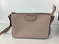 Front and side view of the blush pink DKNY leather purse showing overall shape, zipper top, and adjusted strap.