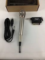 Setup of silver Hisonic microphone with mesh grille, black cable, wireless receiver, and battery displayed on white background