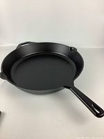 Full side view of the round cast iron skillet showing handle and spouts.