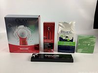 Lot of new beauty products including boxed Olay Regenerist Facial Cleansing Brush, L'Oreal eye cream, Biore pore strips, Mediheal green tea mask, and Owude eyeliner.