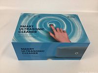 Original boxed packaging of Alnec Smart Ultrasonic Cleaner showing product name and branding with a finger pressing a button on a blue water ripple background.