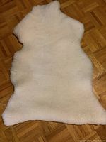 Full view of the natural sheepskin area rug spread flat on a wooden floor showing its full irregular shape and size.
