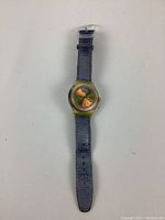 Full view of vintage Swatch automatic wristwatch with blue band laid flat on white surface.