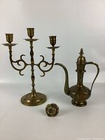 Image showing all three brass items: three-arm candle holder, teapot, and small flower-shaped item.