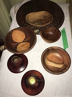 Photo showing four wooden serving bowls and two wooden candlestick holders on a white tablecloth with the large round bread cutting board in the background