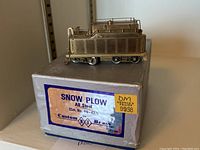 Brass model snow plow on original box with label showing product and brand information