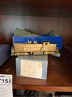 Model brass train on top of original blue and grey box, partially cleaned showing brass finish on the train body.
