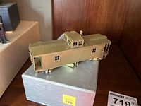 Side view of brass model train car resting on original box with price tag visible