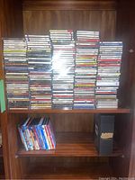 Four stacks of jewel-case CDs on top shelf with a row of DVDs and a binder on the shelf below