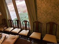 Six wood dining room chairs positioned near windows, seats upholstered in light fabric, wood finish medium brown with moderate wear.