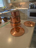 Three copper saucepans stacked on countertop with two copper lids laid out in front