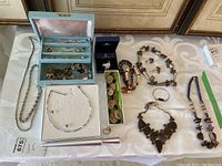 Full overview of the costume jewelry lot showing multiple necklaces, earrings, bracelets, ring, and a jewelry box with compartments containing more jewelry pieces.