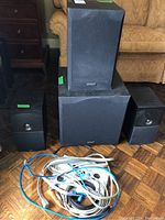 Energy speaker system including subwoofer, amplifier, two speakers, and cables arranged on wooden floor in front of sofa and side table.