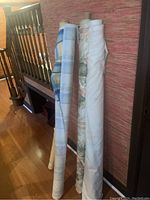 Four bolts of fabric standing upright showing different patterns and colors including a blue and light-colored fabric.