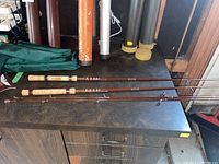 Two Fenwick fishing rods laid flat on table next to cylindrical rod cases of various colors