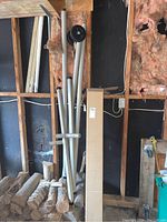 Photo showing bundled tubular metal frame parts and a cardboard box standing against a wall with exposed wooden studs and insulation.