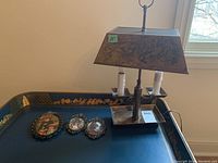 Photo showing metal lamp with patina, rectangular tapered shade and three framed prints on decorative tray.