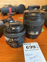 Both Nikon lenses on wooden table with MaxSold lot tag