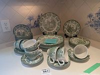 Overview of entire collection arranged on counter, showing bowls, teacups, saucers, salad plates, and dinner plates with green scenic Olde Inns transferware decoration