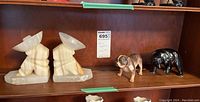 Pair of onyx bookends with a seated figure wearing wide-brimmed hats, showing natural stone banding and coloration, along with a Royal Doulton ceramic bulldog and a black bear figurine beside them on a wooden shelf.