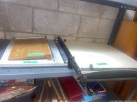 View of three paper cutters on shelf, 10 inch and 12 inch cutters showing measuring grids and blades