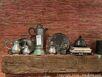 Full lot showing all pewter items and books arranged on wooden beam against red textured background.