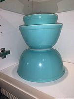 Stacked view of three turquoise Pyrex mixing bowls inside a cabinet shelf.