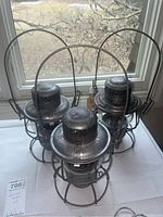 Three metal railway lamps grouped on tabletop in front of window