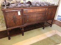 Front view of the antique wooden sideboard showing three drawers and two cabinet doors with decorative metal handles. The top surface holds crystal dishware, which is not included.