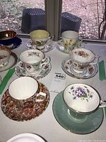 Photo shows six sets of teacups and saucers of varying floral patterns and colors on a table, illustrating the full lot.