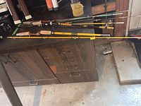 Top-down view of three fishing rods with distinctive handles and colors on a garage floor