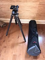 Full view of Manfrotto 410 tripod standing with extended legs and carrying bag lying on the floor next to it on wood floor